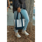 Person holding a tote bag by a tree on a sidewalk