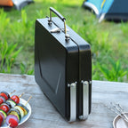 Black portable grill on a wooden table with skewered vegetables and a plate in the background.