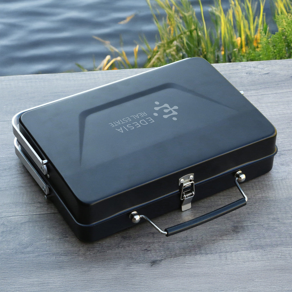 Black metal grill with a visible brand logo on a wooden surface near water.