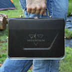 Person holding a black briefcase with 'Mountain' branding outdoors.