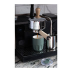 A black espresso machine with a stainless steel portafilter and wooden handle dispensing coffee into an Olla 10 oz Vacuum Coffee Cup with Ceramic Liner
