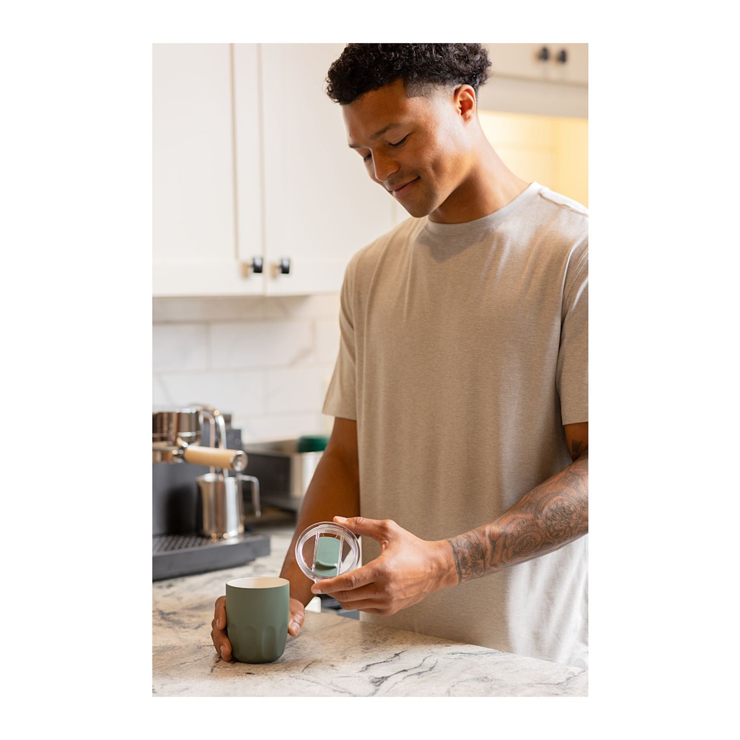 A man in a beige t-shirt stands in a kitchen, holding a Olla 10 oz Vacuum Coffee Cup with Ceramic Liner