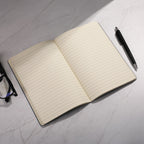 Open notebook with lined pages on a marble surface, accompanied by a pen and glasses.