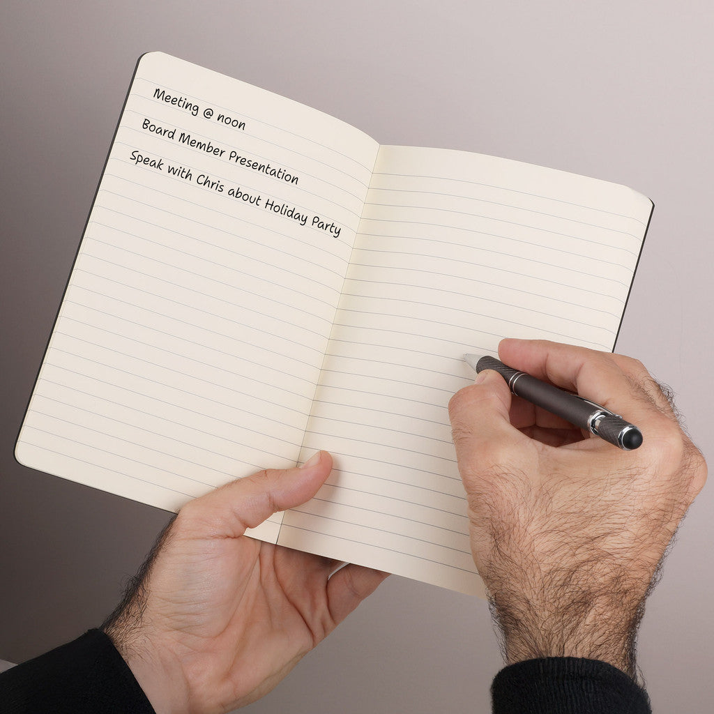 Hand holding a pen over an open notebook with handwritten notes on a plain background
