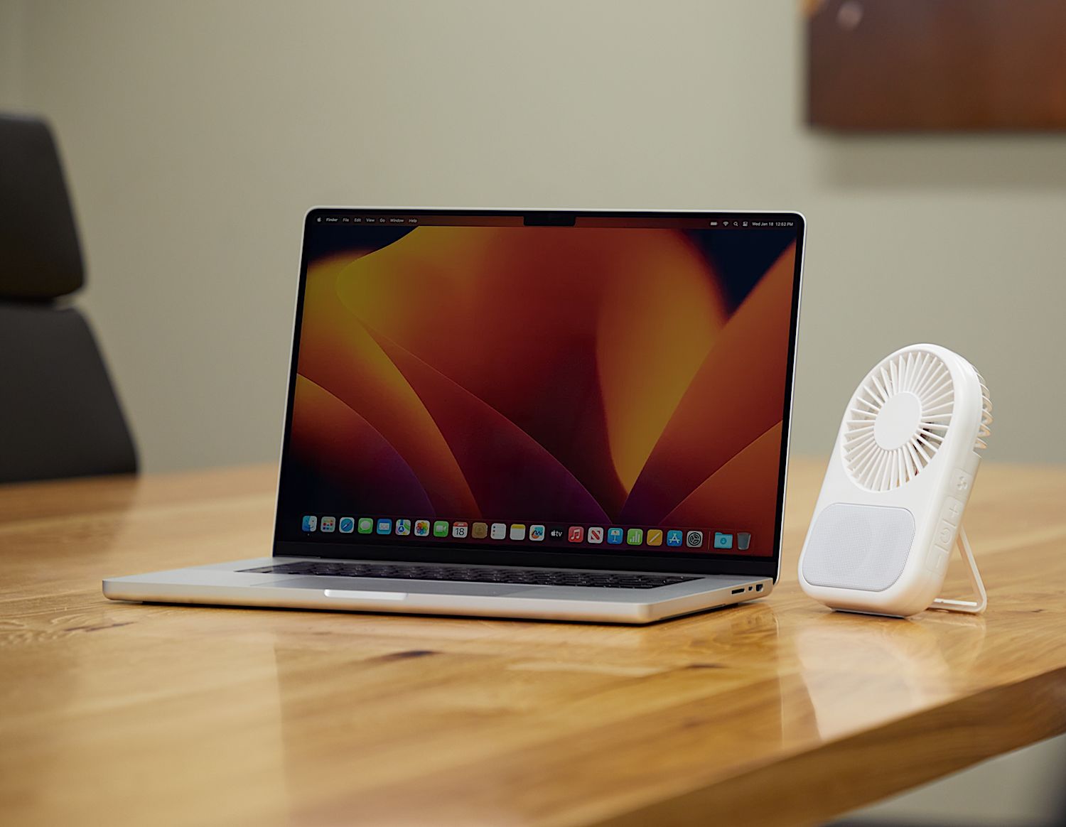 Laptop on a wooden table with a small white fan next to it