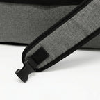 Close-up of a gray and black textured shoulder strap with a black plastic buckle, resting on a white surface.
