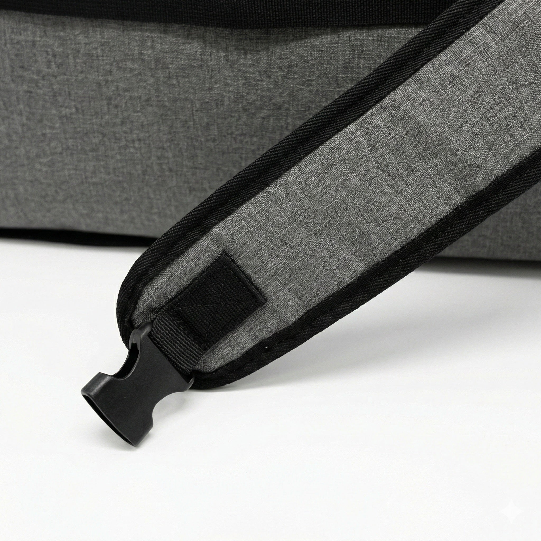 Close-up of a gray and black textured shoulder strap with a black plastic buckle, resting on a white surface.