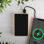 Rectangular wooden power bank charging a smartphone with a green charging indicator on a light background.