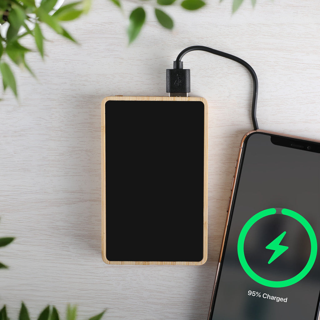 Rectangular wooden power bank charging a smartphone with a green charging indicator on a light background.