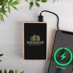 Portable power bank with  logo charging a smartphone on a light surface with greenery.