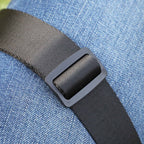 Close-up of a black adjustable web belt with a matte black plastic buckle, worn over blue denim fabric.