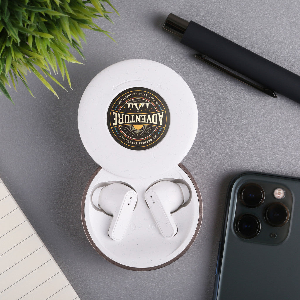 White wireless earbuds in a charging case on a gray surface with a phone and pen.