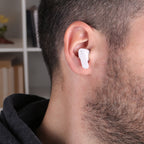 White wireless earbud in a person's ear with a blurred indoor background