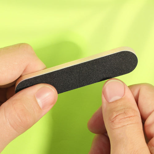 Hand holding a nail file against a green background