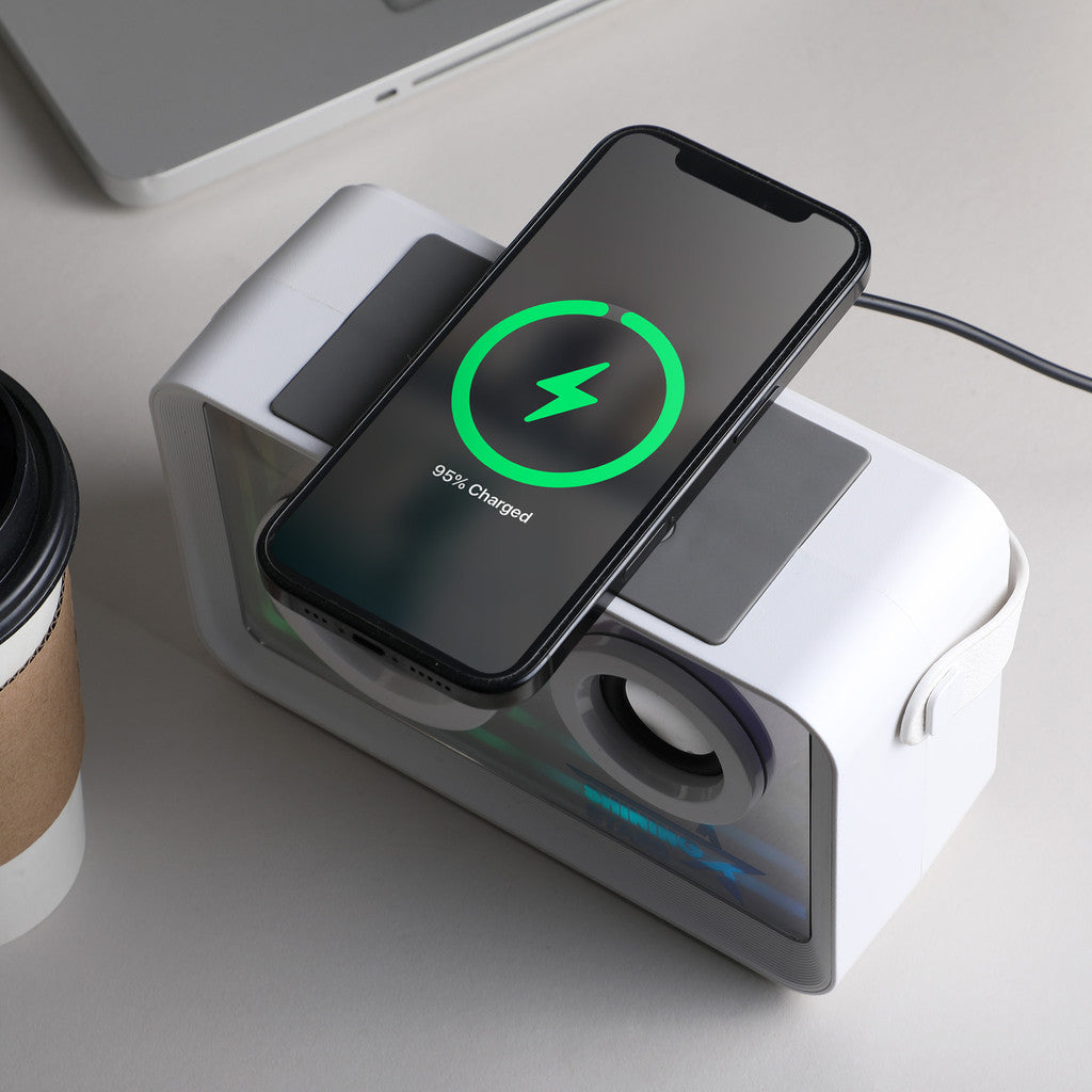 Smartphone charging on a multi-device charging station with a laptop and coffee cup in the background.