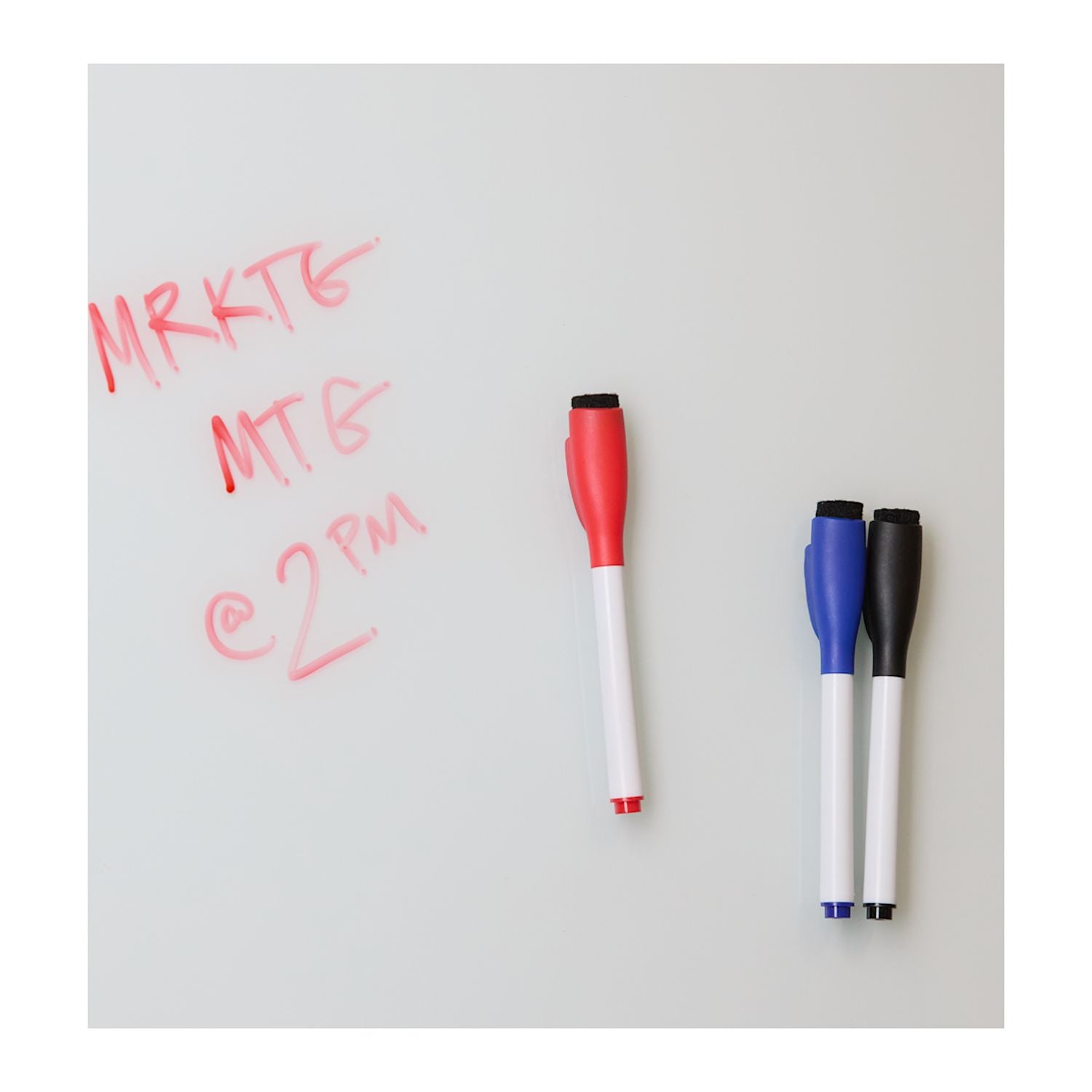 Three markers with red, blue, and black caps on a whiteboard with red writing.