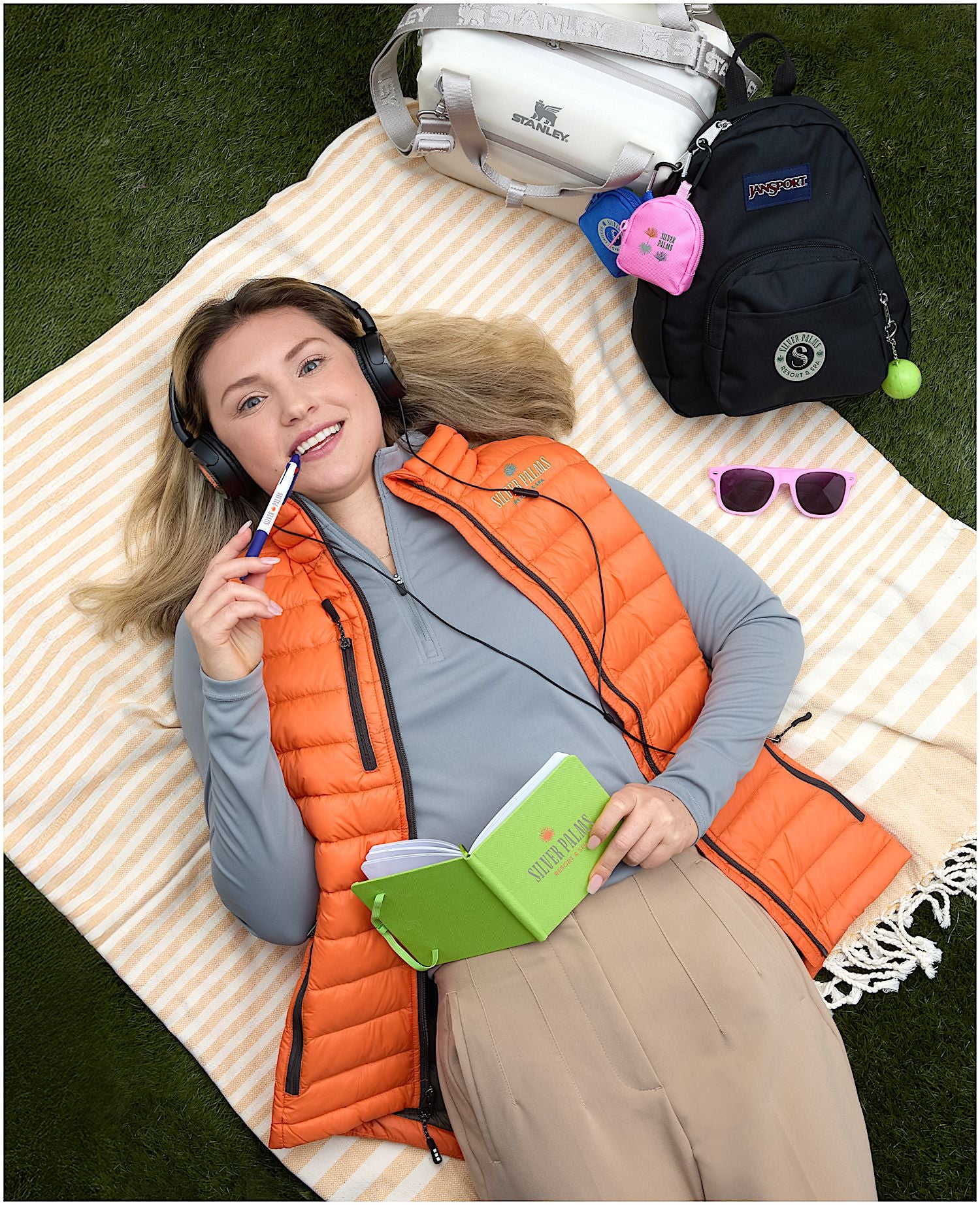 Woman lying on a blanket with headphones, book, and backpack outdoors