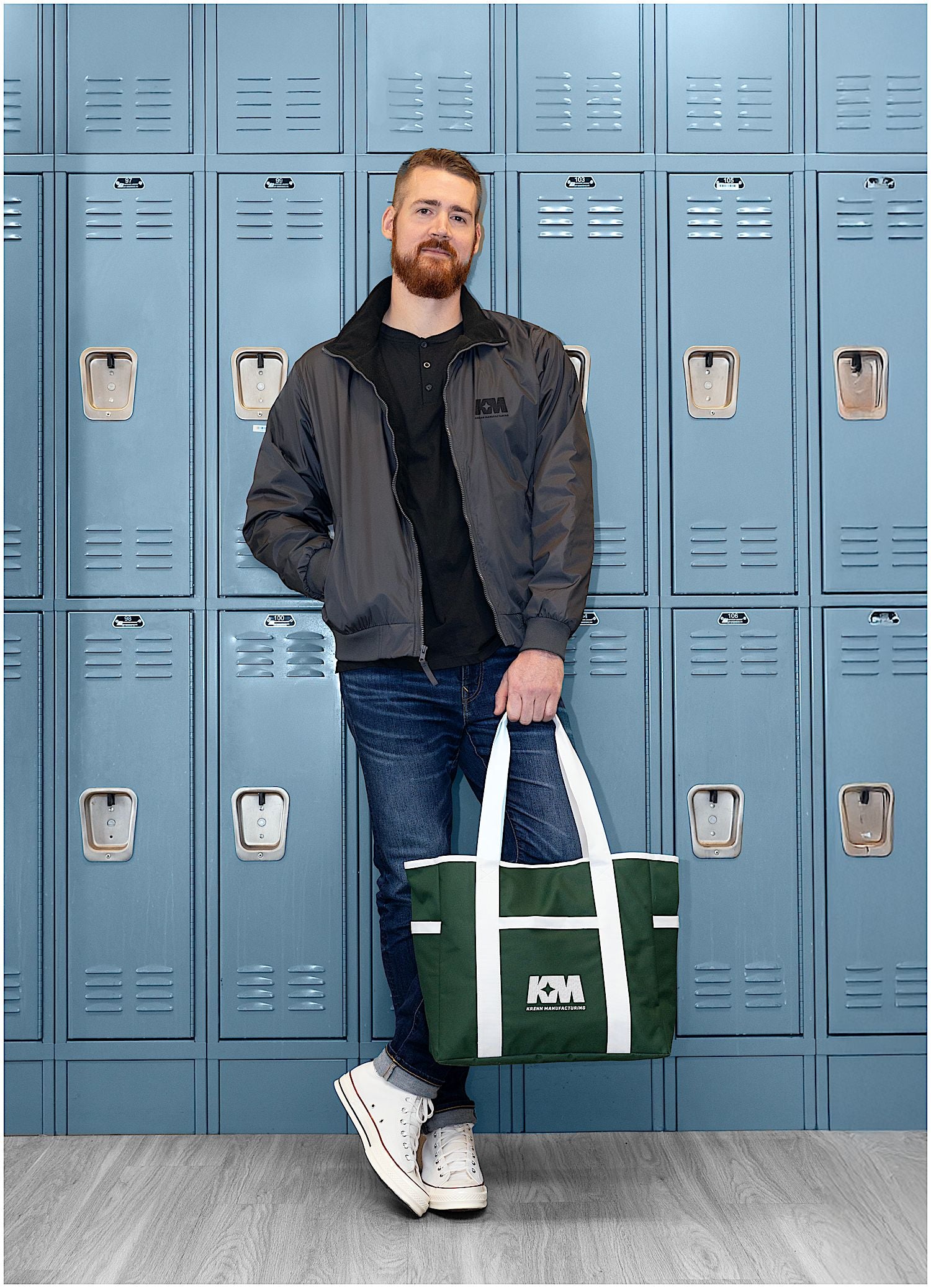 Man holding a green Varsity Club Tote in front of blue lockers