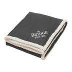 Black blanket with white trim and 'The Bridge House' text on a white background
